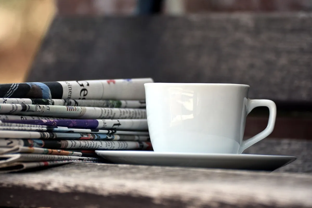 Cup of coffee beside a pile of newspapers and magazines on a wooden table